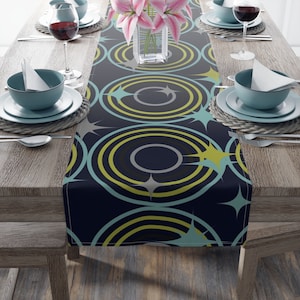 May include: A navy blue table runner with a geometric pattern of concentric circles in shades of teal, yellow, and gray. The circles are accented with gold stars.