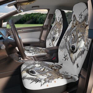 Puede incluir: Fundas de asiento de coche con una ilustración detallada de un lobo en tonos grises, marrones y blancos. El diseño incluye estrellas y un efecto de acuarela, creando un aspecto único y artístico. Las fundas están instaladas en el interior de un coche.