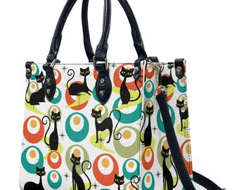 May include: A white handbag with a black handle and strap, featuring a repeating pattern of black cat silhouettes and colorful mid-century modern shapes. The bag has a rectangular shape with black accents.