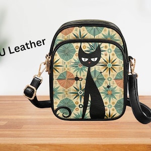 May include: Black crossbody bag with a cat design. The bag features a black cat silhouette on a patterned background with teal, orange, and cream colours. The bag has a black strap and gold-coloured hardware. The text "PU Leather" is visible.