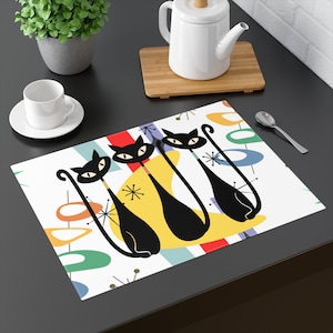 May include: A white placemat with a colourful mid-century modern design featuring three black cats with yellow, blue, green, and red accents.