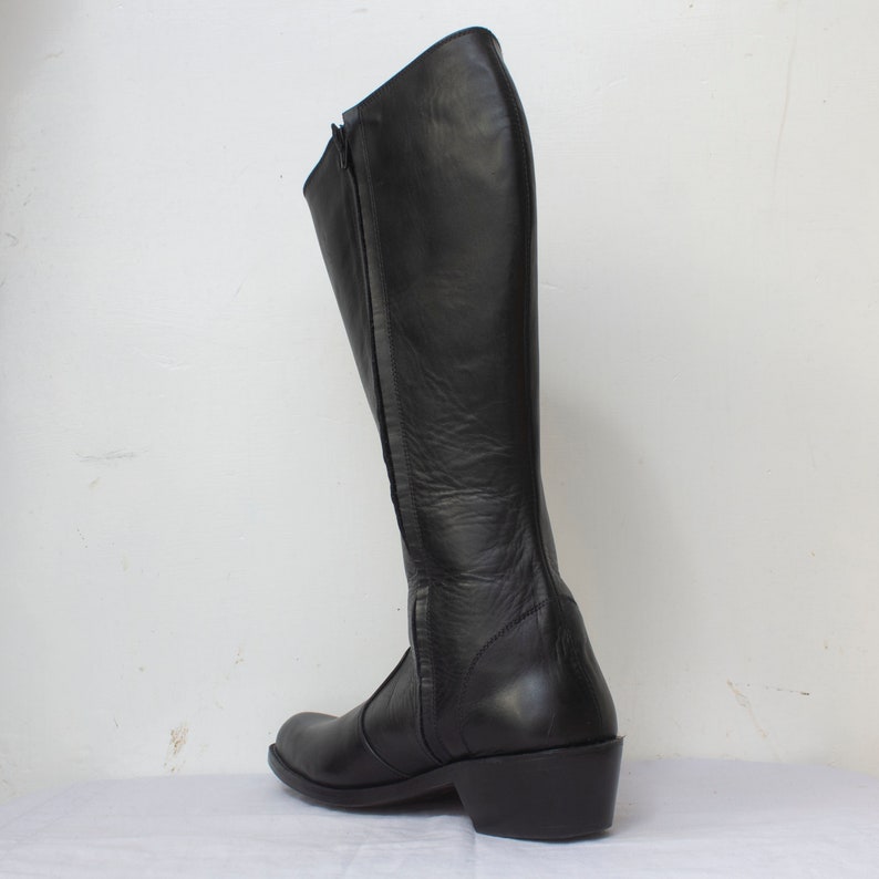 May include: Black leather knee-high boots with a zipper up the back and a low heel.