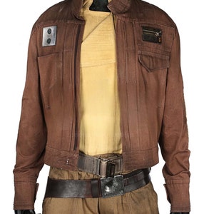 May include: A brown jacket with a zip fastening and two pockets on the chest. The jacket has a patch on the left pocket and a patch on the right pocket. The jacket is worn over a tan shirt and brown trousers with a brown belt.