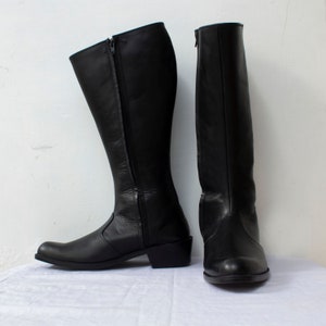 May include: A pair of black leather knee-high boots with a zipper on the inside of each boot.