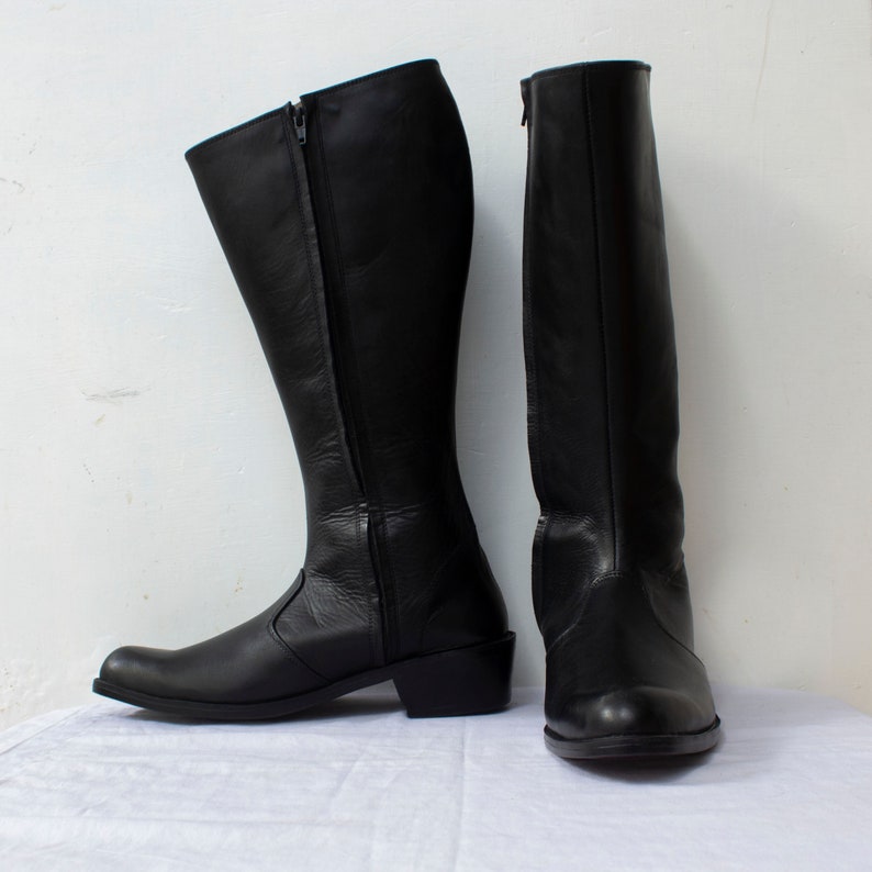 May include: A pair of black leather knee-high boots with a zipper on the inside of each boot.