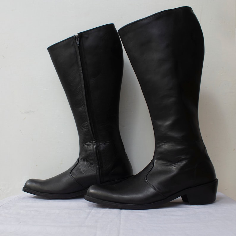 May include: A pair of black leather knee-high boots with a zipper on the inside of each boot. The boots have a low heel.