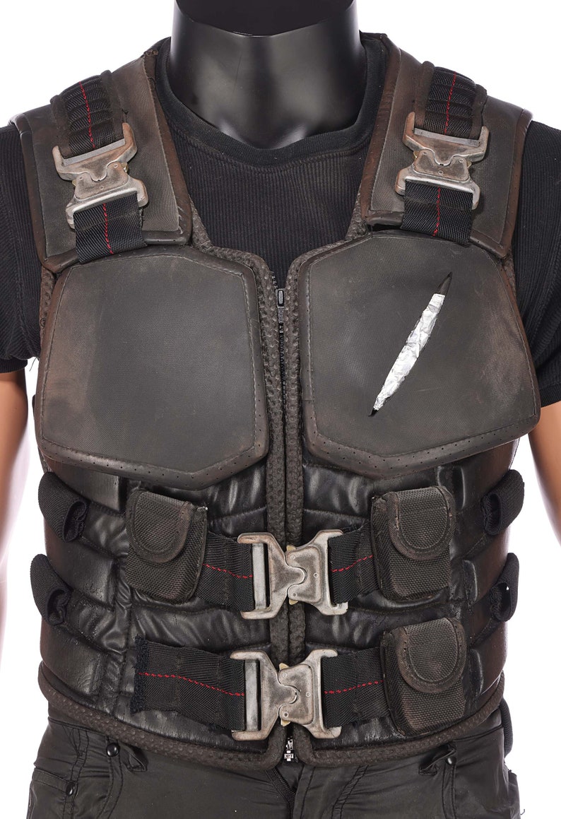 May include: Black tactical vest with multiple straps and buckles. The vest has a zipper closure and a padded front panel. There is a small tear in the front panel.