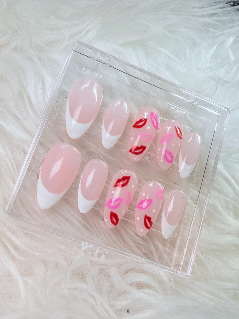 Puede incluir: Un conjunto de diez u&ntilde;as postizas de color rosa y blanco con una punta blanca y un dise&ntilde;o de labios rojos y rosas en algunas de las u&ntilde;as.