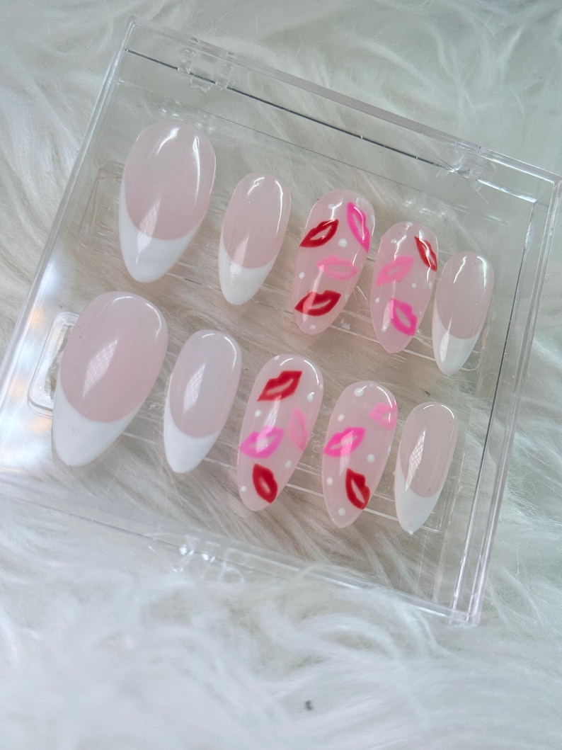 Puede incluir: Conjunto de diez u&ntilde;as postizas ovaladas con punta francesa blanca. Algunas u&ntilde;as tienen un dise&ntilde;o de labios rojos y rosas sobre fondo blanco.
