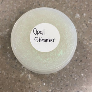May include: A white round container with a clear lid. The lid has a white sticker with the text "Opal Shimmer" written in black.