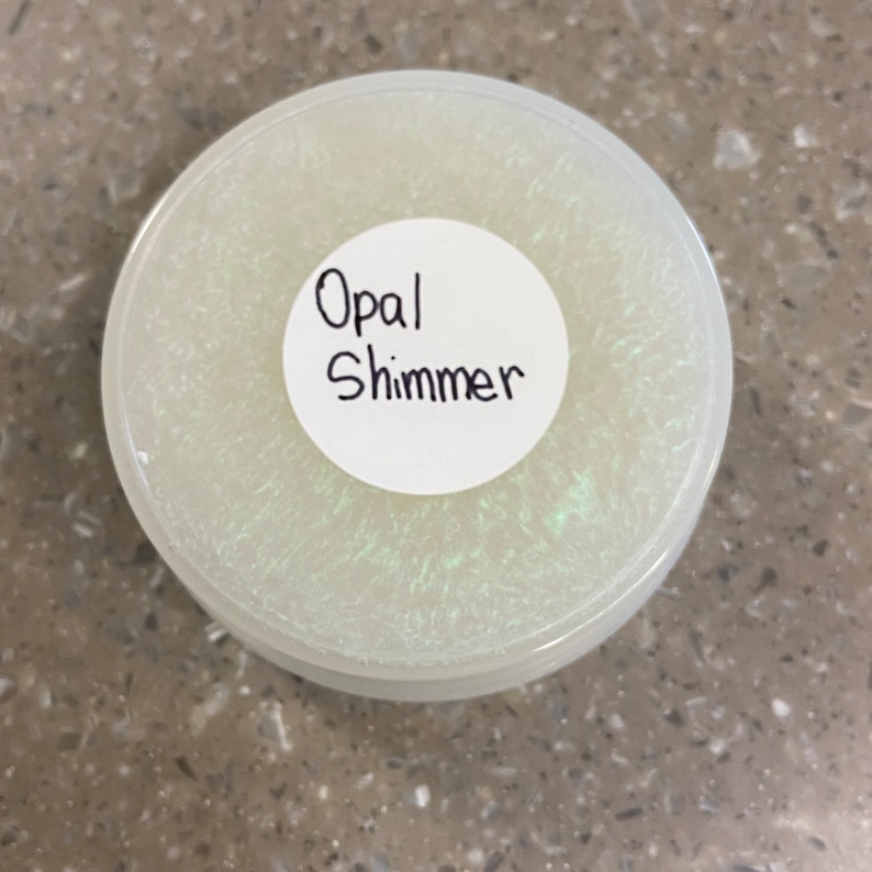 May include: A white round container with a clear lid. The lid has a white sticker with the text "Opal Shimmer" written in black.