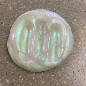 May include: A close-up of iridescent slime with a pearlescent white base and green and blue shimmer.