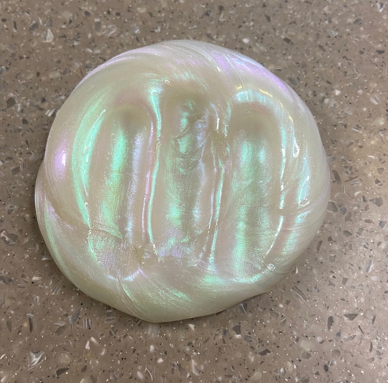May include: A close-up of iridescent slime with a pearlescent white base and green and blue shimmer.