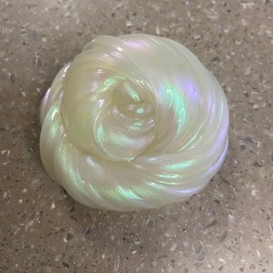 May include: A close-up of a white iridescent slime with a pearlescent sheen. The slime is soft and gooey, and it is shaped like a ball.