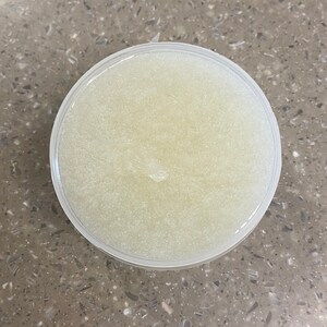 May include: A clear plastic container filled with a white, sparkly sugar scrub.