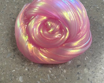 Puede incluir: Primer plano de una slime rosa con brillo iridiscente. La slime tiene forma de bola y una textura lisa y brillante.