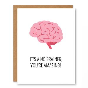 Könnte beinhalten: Eine Grußkarte mit braunem Rand und weißem Innenraum. Die Karte zeigt eine rosa Gehirnillustration und den Text "IT'S A NO BRAINER, YOU'RE AMAZING!" in schwarzer Schrift.