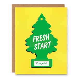 Peut inclure: Carte de vœux avec un fond jaune et un motif de désodorisant vert. Le désodorisant porte les mots "FRESH START" en blanc, et le mot "Congrats!" est en bas. La carte est posée sur un fond marron.