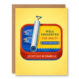 Peut inclure: Carte de vœux avec un fond jaune et une illustration de boîte de sardines. La boîte rouge contient deux poissons bleus. Le texte sur la boîte indique « BIEN CONSERVÉ, DE QUALITÉ SUPÉRIEURE » et « ÂGE NET 40 ANS ».
