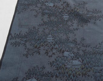 May include: A long, rectangular textile runner in shades of dark blue and charcoal gray. The fabric features a woven pattern depicting a landscape with small buildings, pagodas, and dense clusters of trees arranged in a repeating, flowing design.