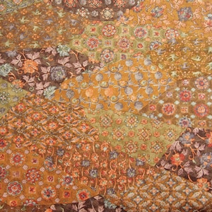 Peut inclure: Gros plan sur un textile patchwork avec des motifs floraux dans les tons marron, orange, vert et bleu. Le design est composé de formes géométriques irrégulières, créant une surface texturée et détaillée.