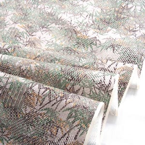May include: Close-up of folded fabric featuring a repeating pattern of green, brown, and white botanical elements. The fabric has a textured appearance, with a mix of small and large shapes. The design is reminiscent of leaves and branches.