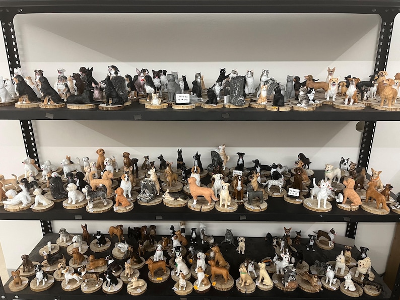 May include: A display of dog ornaments on shelves. The ornaments depict various dog breeds and sizes, each mounted on a small wooden base. The dogs are painted in realistic colours and poses.