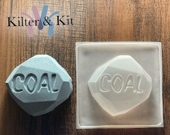 May include: A gray, 3D printed, rock-shaped mold with the word "COAL" embossed on it. The mold is next to a clear plastic mold with the same design.