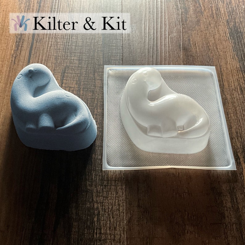 May include: A light blue dinosaur-shaped mold and a white dinosaur-shaped mold. The molds are made of silicone and are used for making soap, candles, or other crafts.