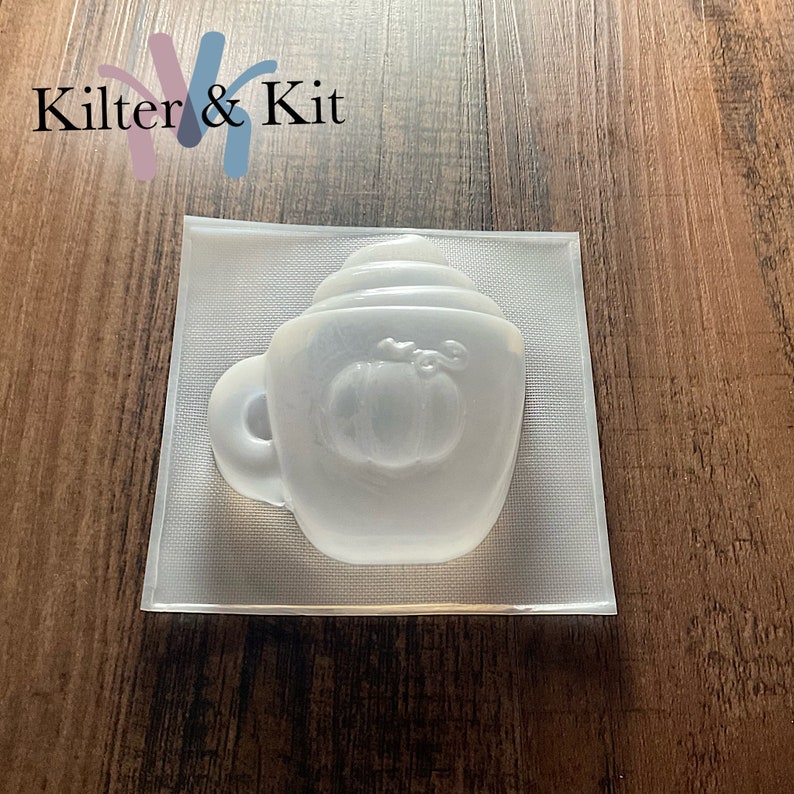 May include: A clear plastic mold for making a pumpkin spice latte soap or candle. The mold is shaped like a coffee mug with a pumpkin design on the front.