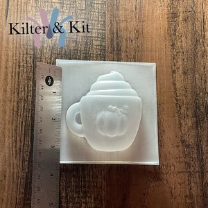 May include: White plastic mold for making a pumpkin spice latte soap or candle. The mold is shaped like a coffee cup with whipped cream on top and a pumpkin in the center.