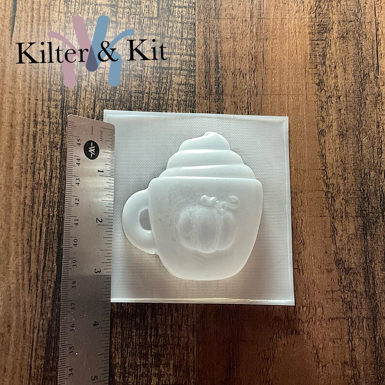 May include: White plastic mold for making a pumpkin spice latte soap or candle. The mold is shaped like a coffee cup with whipped cream on top and a pumpkin in the center.