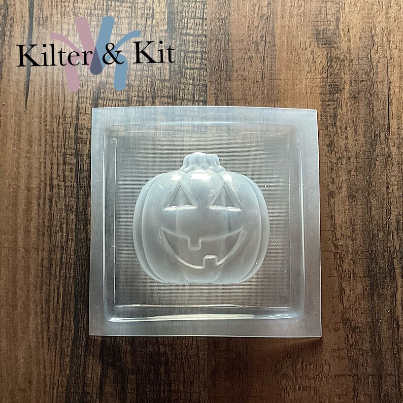 May include: Clear plastic mold for making a pumpkin-shaped soap or candle. The mold is square and has a raised design of a pumpkin with a smiling face.