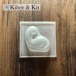 May include: A clear plastic mold shaped like a dinosaur. The mold is designed for making crafts or soap.