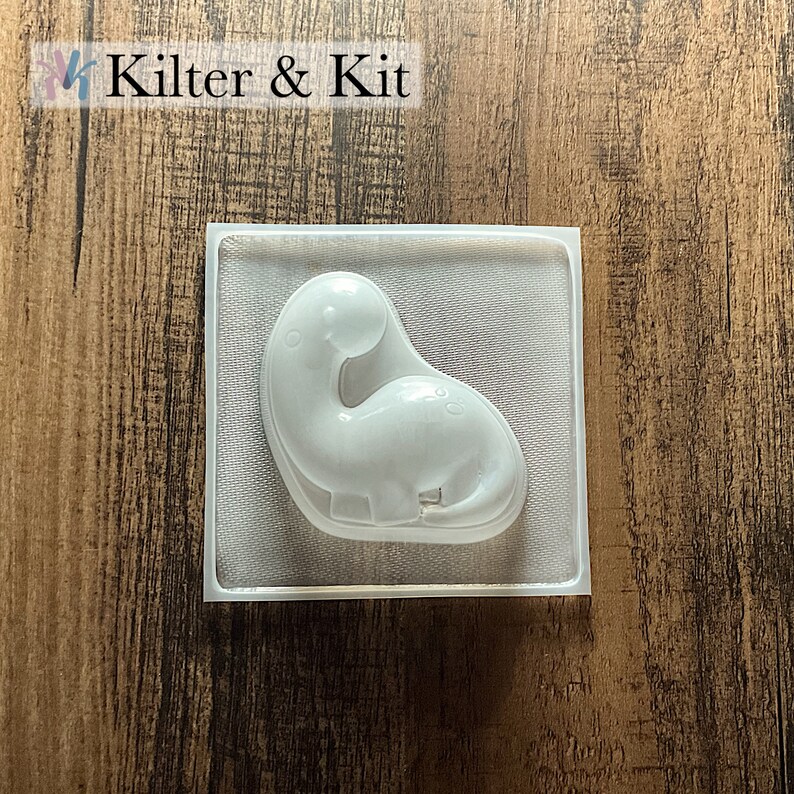 May include: A clear plastic mold shaped like a dinosaur. The mold is designed for making crafts or soap.