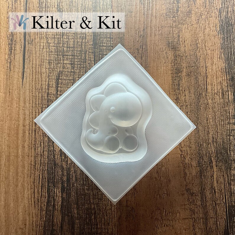 May include: Clear plastic mold shaped like a cartoon dinosaur. The mold is on a wood background.