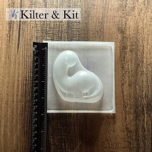 May include: Clear plastic mold for making a dinosaur-shaped object. The mold is approximately 3 inches wide and 4 inches tall.