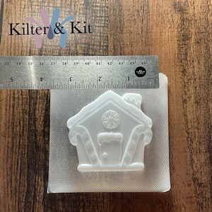 Puede incluir: Molde de pl&aacute;stico blanco de una casa de jengibre con detalles de bast&oacute;n de caramelo. El molde mide aproximadamente 5 cm de alto y 5 cm de ancho.