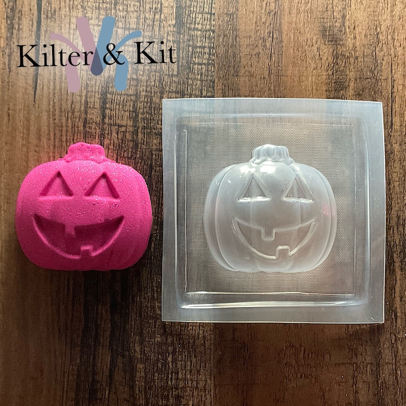 May include: A clear plastic mold of a pumpkin with a smiling face. A pink pumpkin with a smiling face is next to the mold.