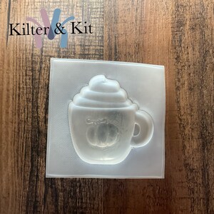 May include: A clear plastic mold for making a pumpkin spice latte soap or candle. The mold is shaped like a coffee cup with whipped cream and a pumpkin on the side.
