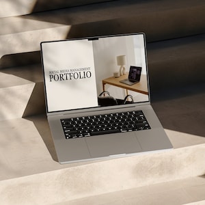 May include: A silver laptop computer open on a concrete staircase. The screen displays a website with the text "Social Media Management Portfolio".