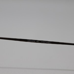 May include: Close-up of the arm of a pair of glasses with the text "UNISEX 80 24074001" printed on it.