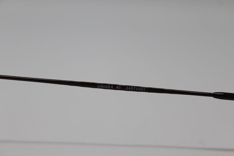 May include: Close-up of the arm of a pair of glasses with the text "UNISEX 80 24074001" printed on it.