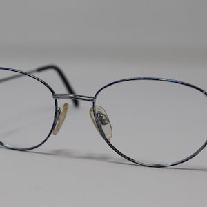 May include: Silver-toned metal eyeglasses with a blue and silver patterned frame. The glasses have oval lenses.