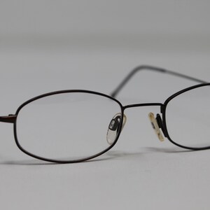 May include: A pair of black metal eyeglasses with oval-shaped lenses. The glasses have a simple, classic design.