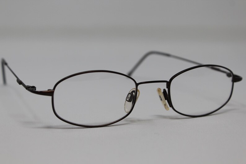 May include: A pair of black metal eyeglasses with oval-shaped lenses. The glasses have a simple, classic design.