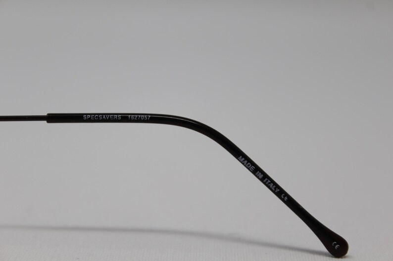 May include: Close-up of the black arm of a pair of glasses with the text "SPECSAVERS 1827057" and "MADE IN ITALY CE" printed on it.