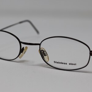 May include: Black oval-shaped eyeglasses with a stainless steel frame.