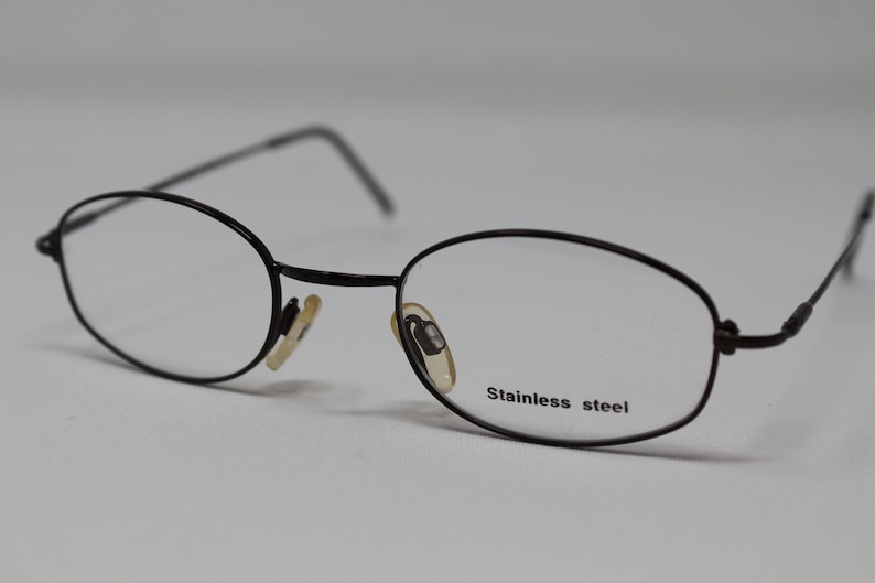 May include: Black oval-shaped eyeglasses with a stainless steel frame.
