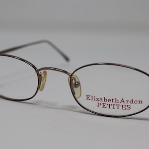 May include: A pair of brown metal eyeglasses with oval lenses. The brand name "Elizabeth Arden PETITES" is printed on the right lens.